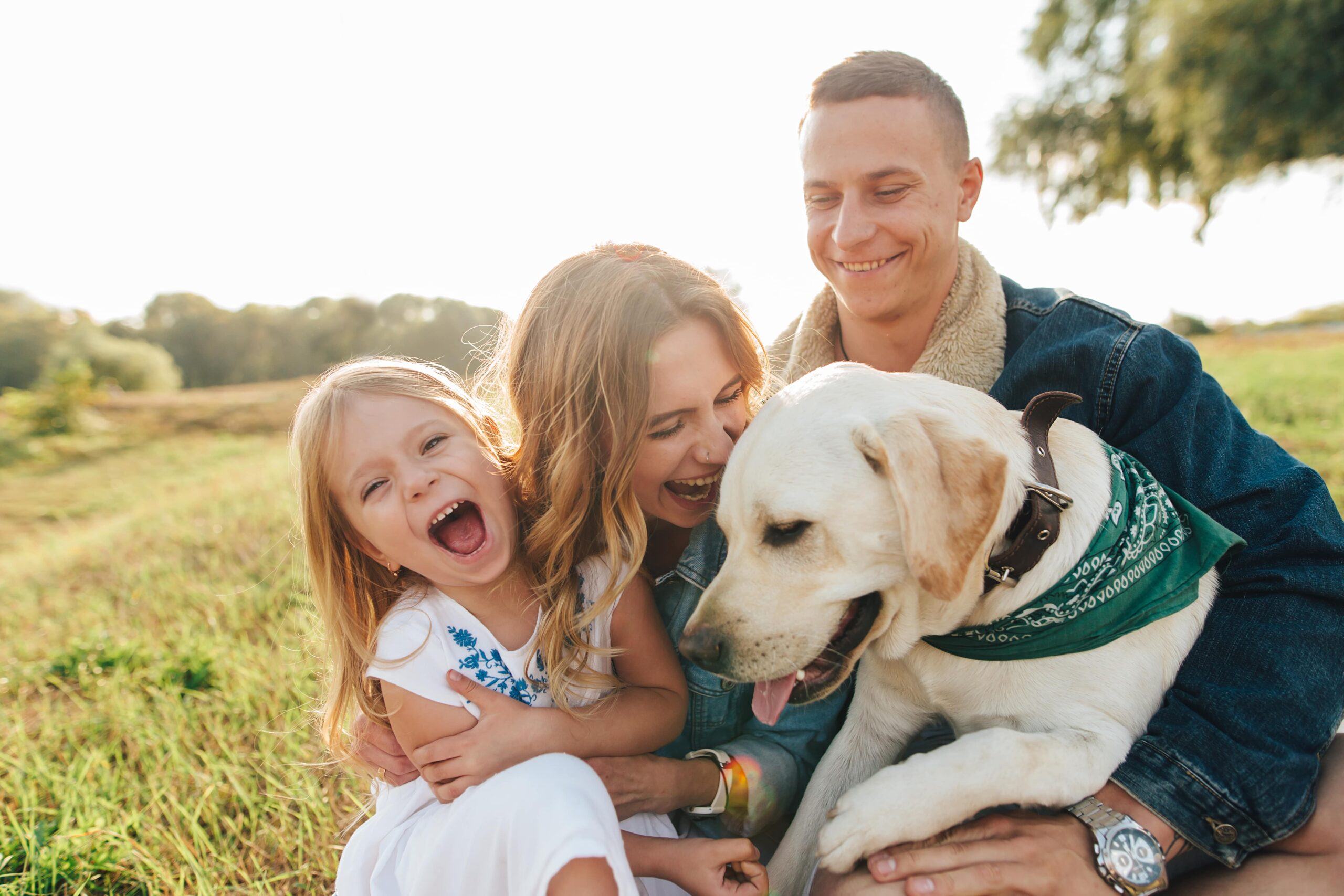 family smiling with their dog in a park