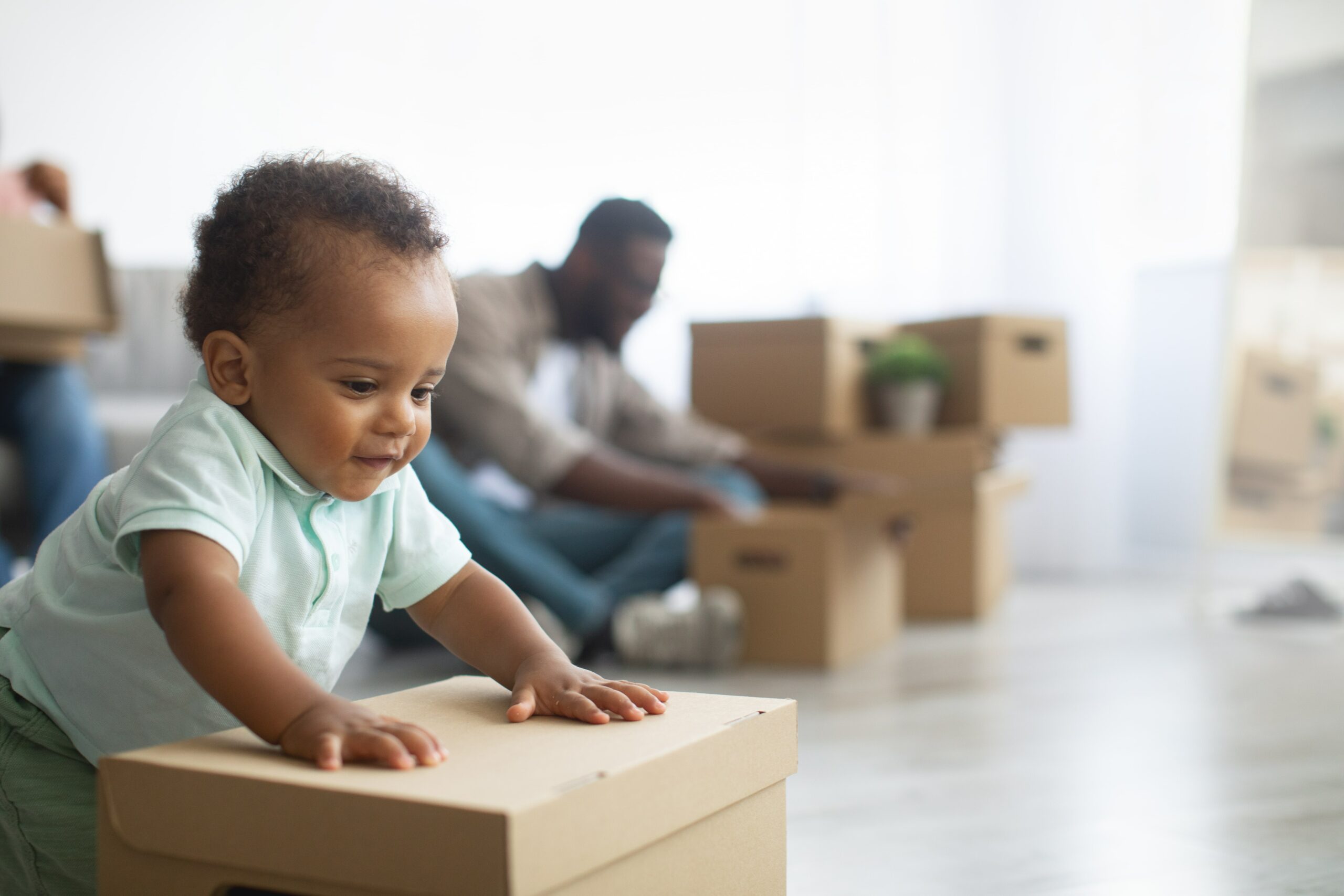 toddler playing with a moving box while the rest of the family is packing boxes